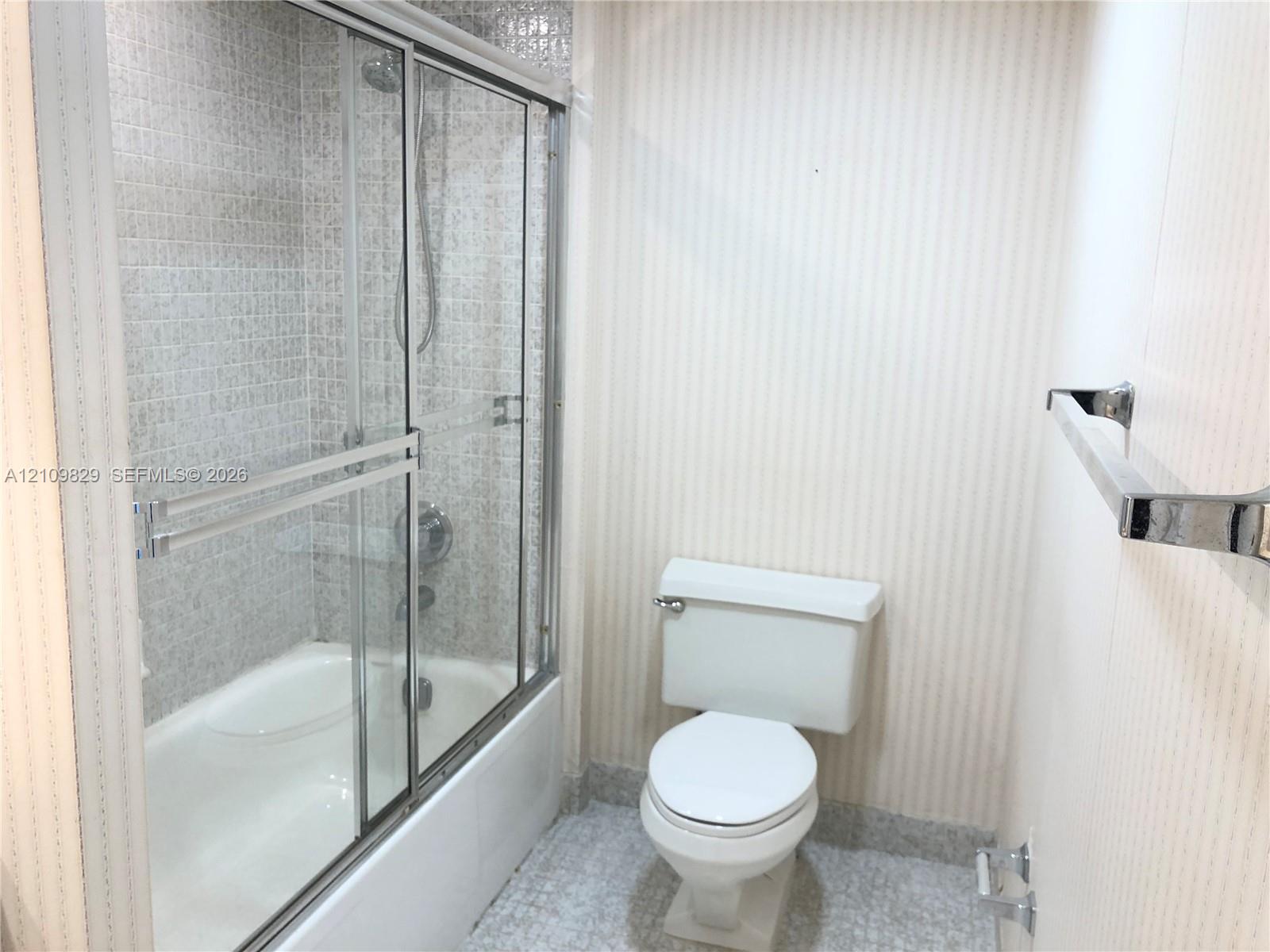 Shower-tub combination featuring a sliding glass enclosure, integrated chrome fixtures, mosaic-tiled shower surround, and a wall-mounted chrome towel bar