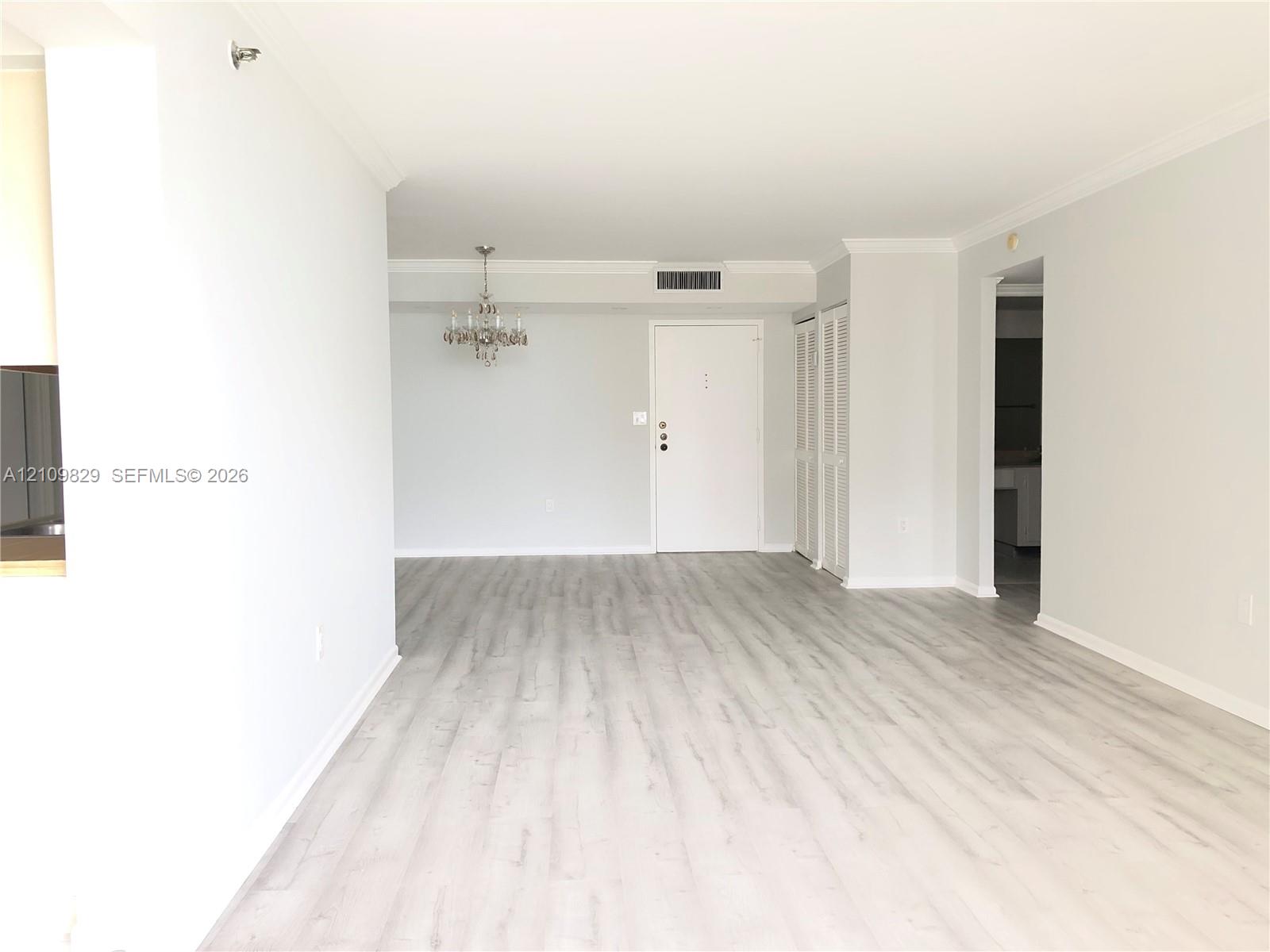 Open-concept interior featuring wood-finish flooring, crown molding, a decorative chandelier, and floor-to-ceiling louvered-door closets