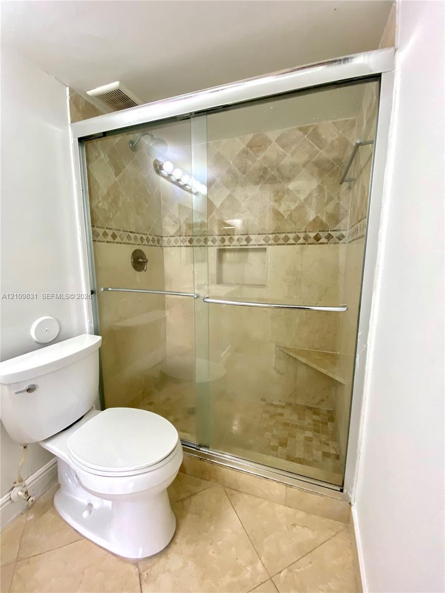 Walk-in shower featuring a sliding glass enclosure, stone-tiled walls with a decorative accent border, a built-in corner bench, a recessed wall niche, and stone-finish floor tile