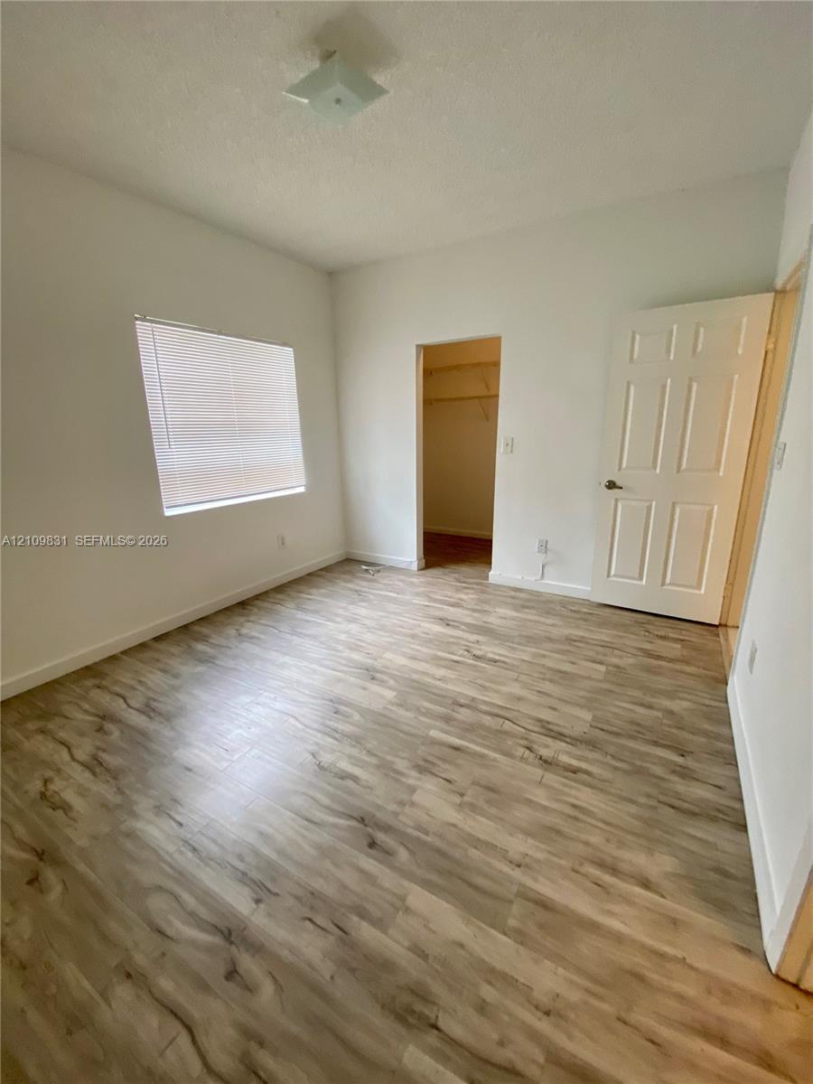 Room featuring wood-finish flooring, a flush-mount ceiling light, a window with horizontal blinds, and a built-in closet with shelving