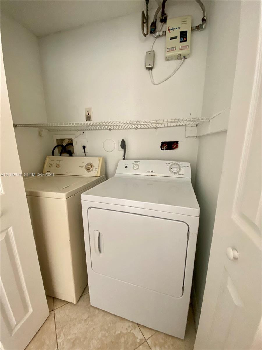 Laundry closet featuring tile flooring, white-finish cabinetry and walls, and integrated shelving