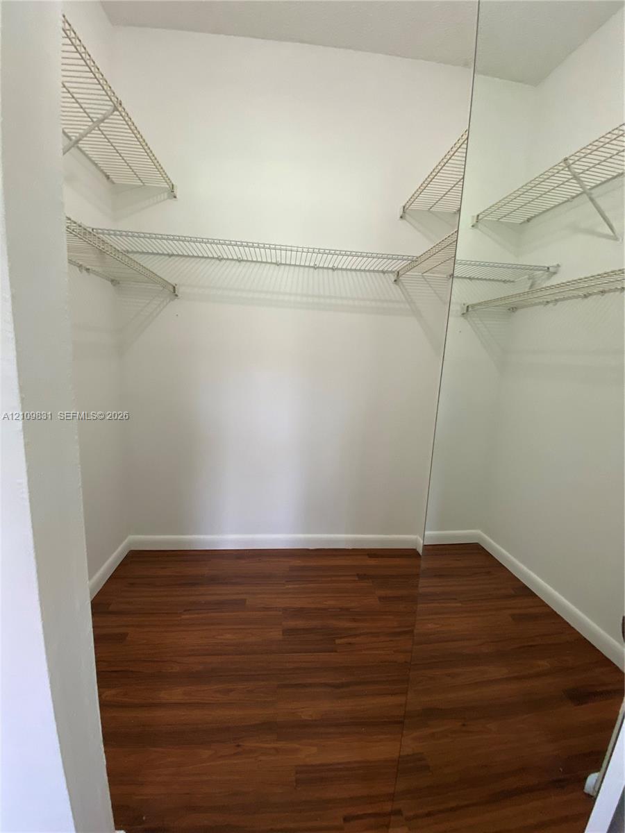 Walk-in closet featuring wood-finish flooring, full-height mirrored door panels, and tiered wire shelving