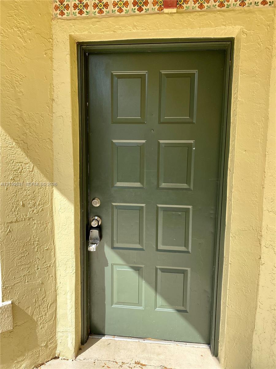Eight-panel entry door featuring a matte green finish, textured stucco exterior walls, and decorative patterned tile trim Eight-panel entry door featuring a matte green finish, textured stucco exterior walls, and decorative patterned tile trim