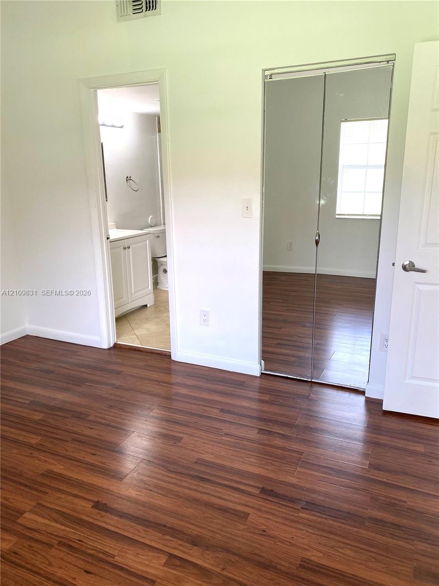 Wood-finish flooring, mirrored sliding closet doors, multi-panel interior door, and white cabinetry