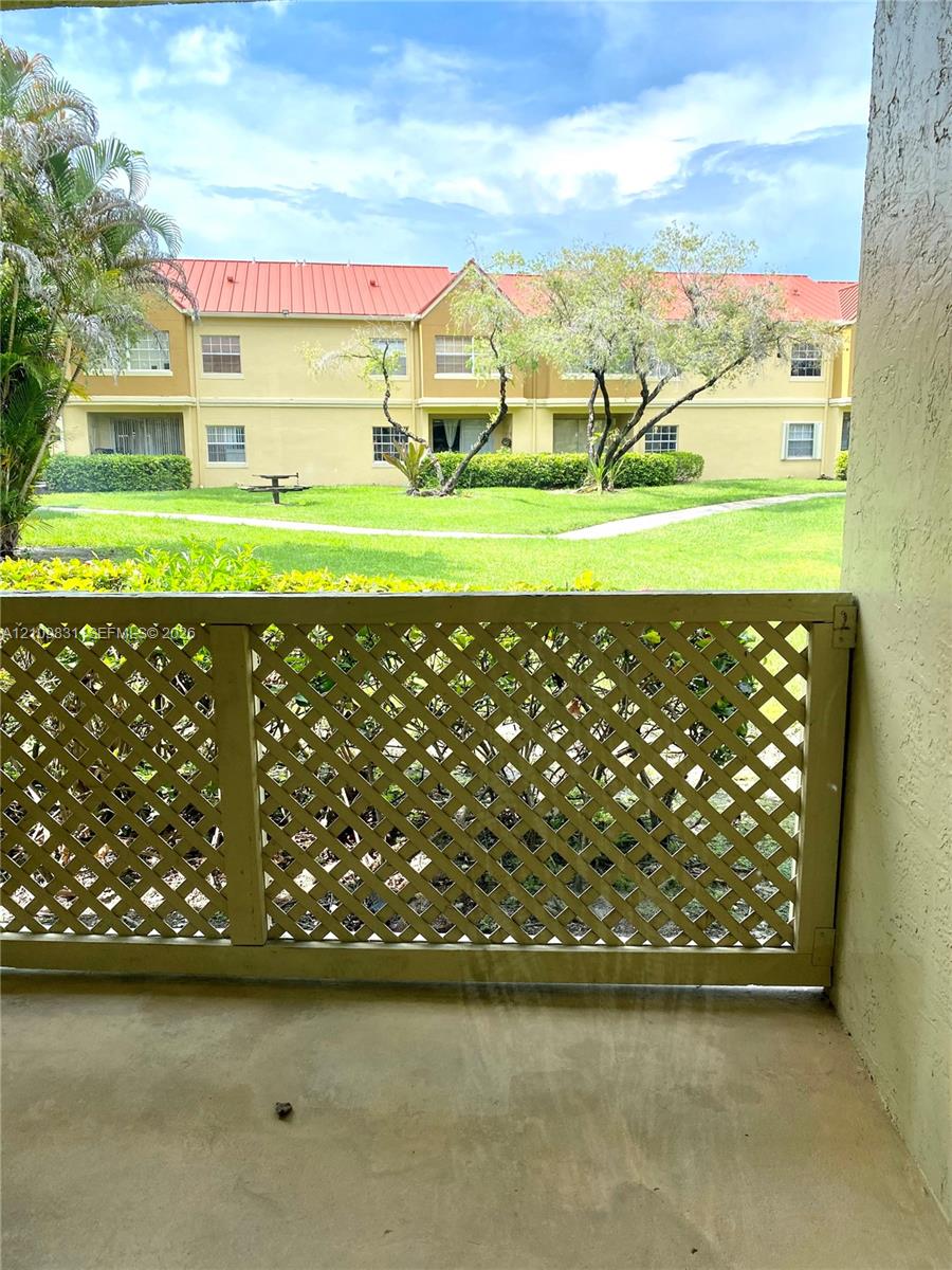 Covered balcony featuring a decorative wood lattice railing, concrete flooring, and greenery Covered balcony featuring a decorative wood lattice railing, concrete flooring, and greenery