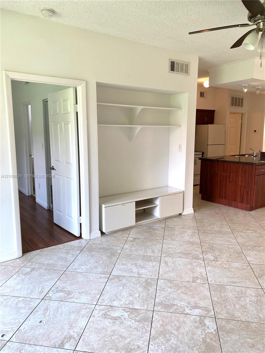 Built-in recessed shelving unit with lower cabinetry, neutral-toned tile flooring, and a ceiling-mounted fan Built-in recessed shelving unit with lower cabinetry, neutral-toned tile flooring, and a ceiling-mounted fan