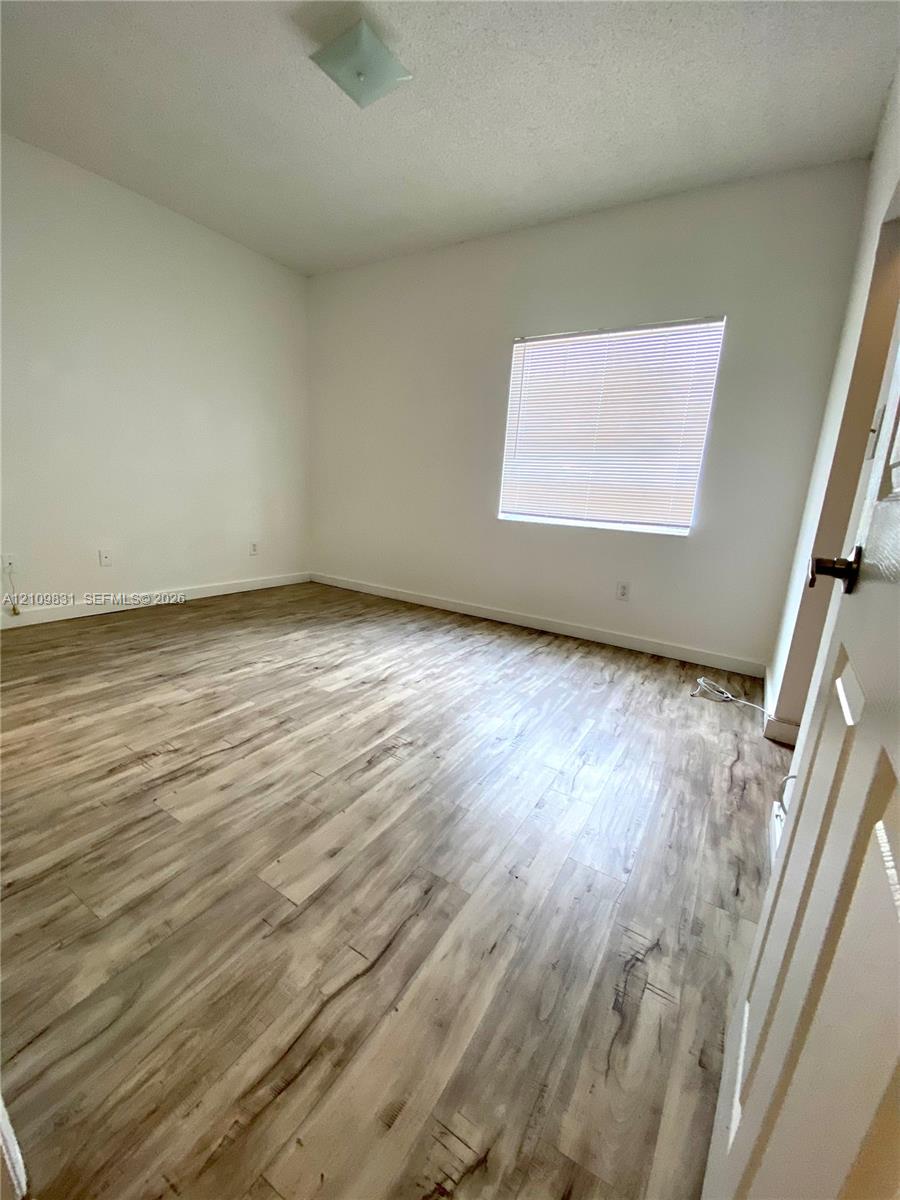 Room featuring wood-finish flooring, neutral walls, a single window, and a flush-mount ceiling light fixture