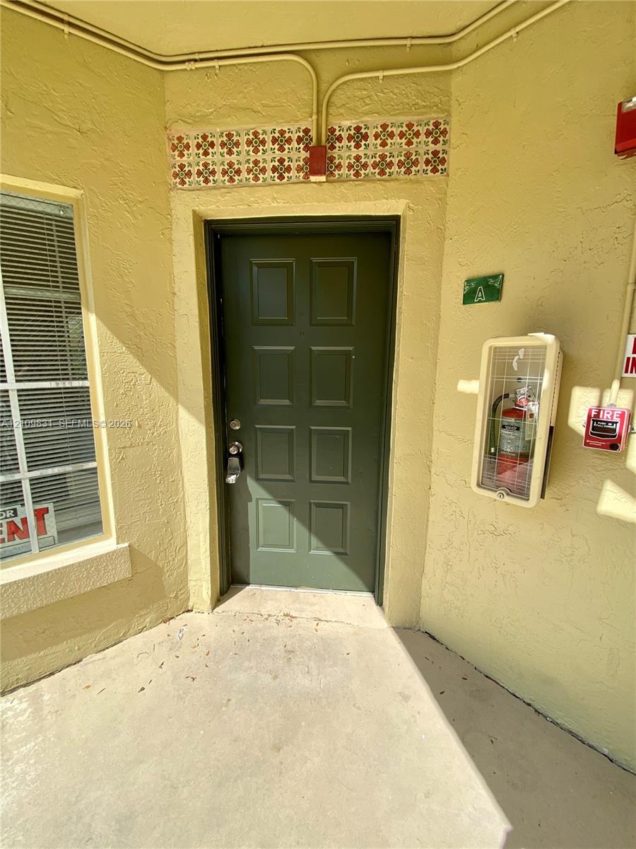 Entrance featuring a paneled olive green door, decorative tile accent trim, and textured stucco exterior finish