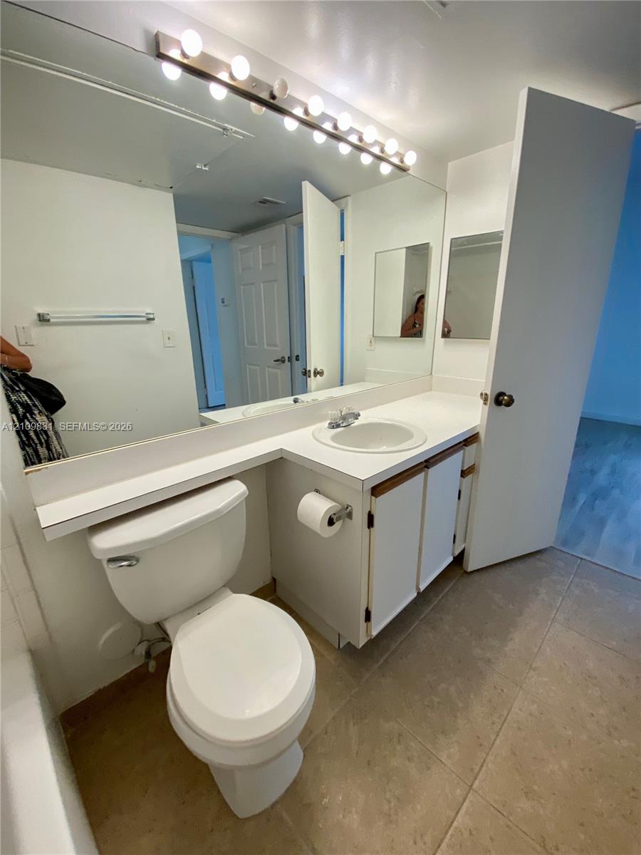 Bathroom featuring a white vanity with a rounded integrated sink, large wall-to-wall mirror, multi-bulb vanity light fixture, and tile flooring