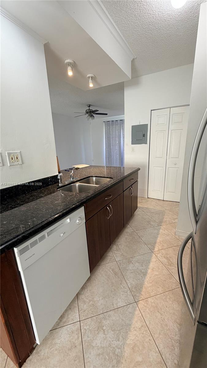 Kitchen featuring dark-toned cabinetry, stone-finish countertops, stainless steel dual-basin sink, tile flooring laid on a diagonal, and built-in dishwasher Kitchen featuring dark-toned cabinetry, stone-finish countertops, stainless steel dual-basin sink, tile flooring laid on a diagonal, and built-in dishwasher