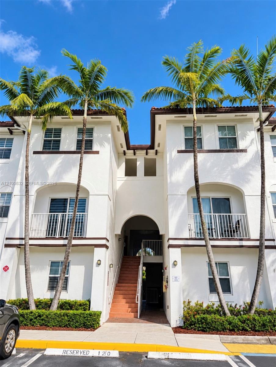 Stucco exterior featuring dual-level balconies with white railings, arched architectural details, and integrated palm tree landscaping Stucco exterior featuring dual-level balconies with white railings, arched architectural details, and integrated palm tree landscaping