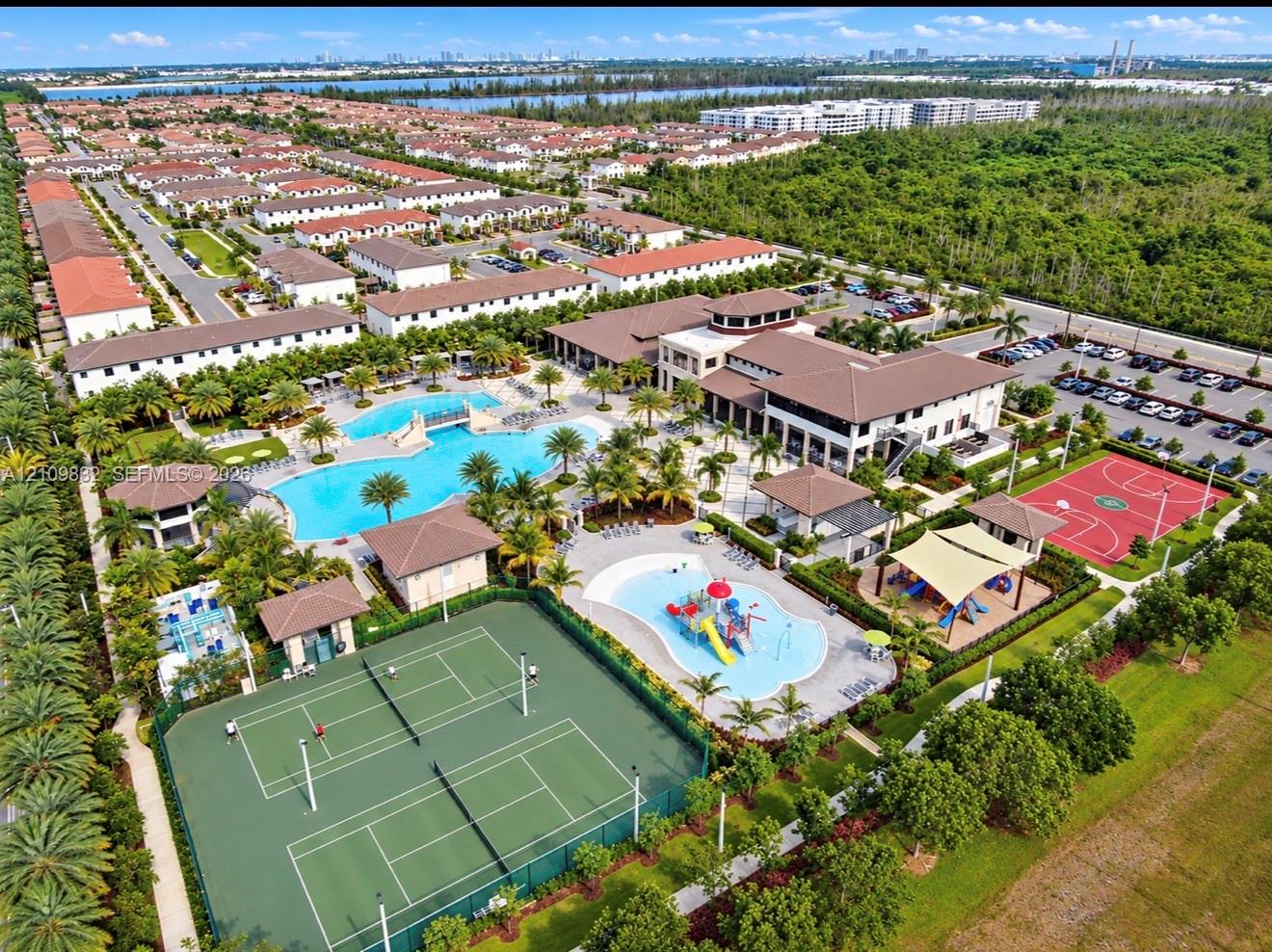 Aerial perspective of a community recreation complex featuring swimming pools with bridge and splash features, tennis courts, basketball court, and clubhouse facility