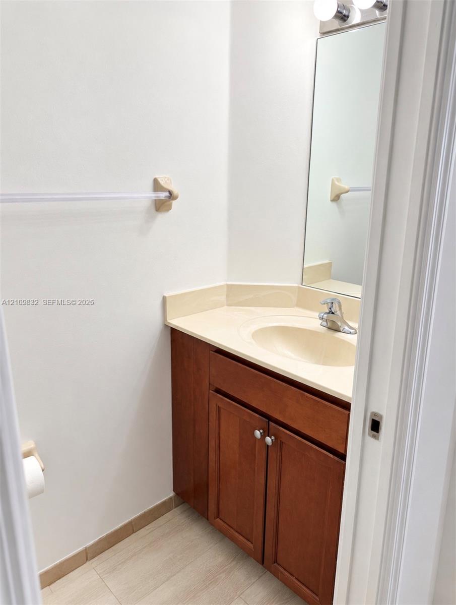 Wood-finish cabinetry, solid-surface countertop with integrated oval basin, polished chrome faucet, rectangular wall-mounted mirror, and multi-light fixture