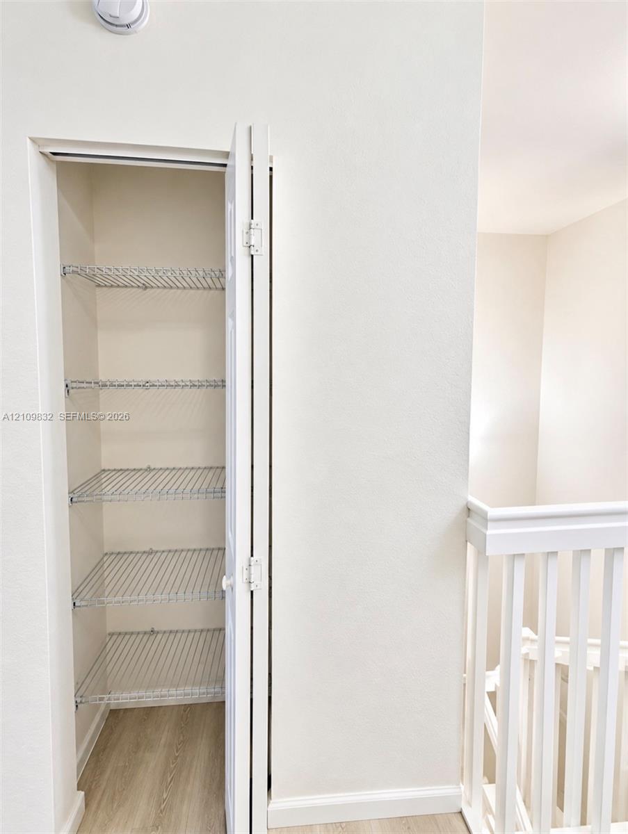 Storage closet featuring bi-fold doors, five tiers of wire shelving, and wood-finish flooring, accompanied by a white baluster railing
