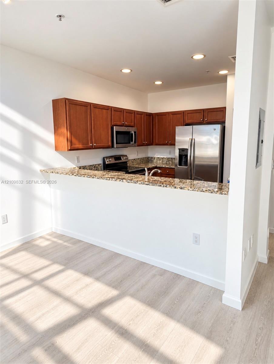 Kitchen featuring a peninsula with a stone countertop, wood-finish cabinetry, stainless steel appliances, and recessed lighting Kitchen featuring a peninsula with a stone countertop, wood-finish cabinetry, stainless steel appliances, and recessed lighting