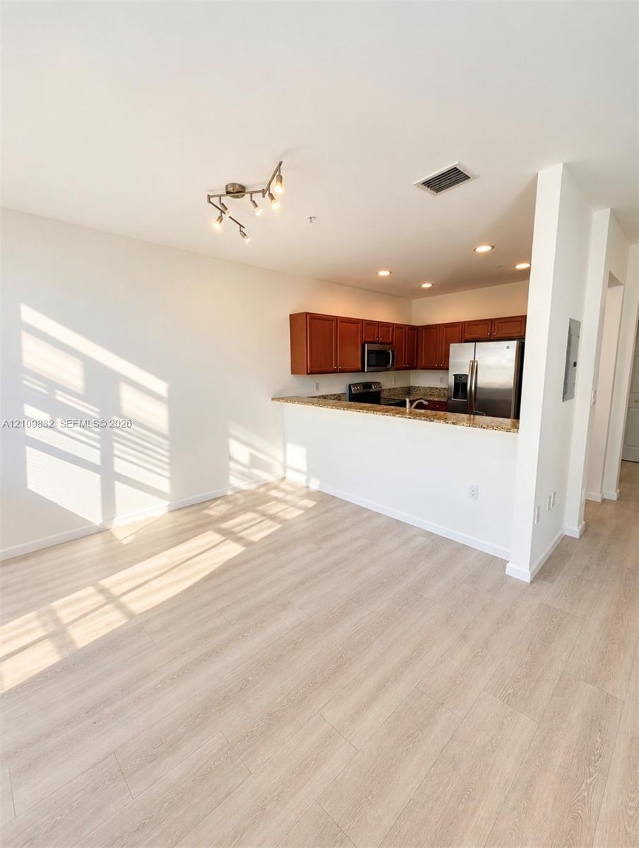 Kitchen featuring wood-finish cabinetry, stone countertops, stainless steel appliances, wood-finish flooring, and multi-directional overhead lighting Kitchen featuring wood-finish cabinetry, stone countertops, stainless steel appliances, wood-finish flooring, and multi-directional overhead lighting