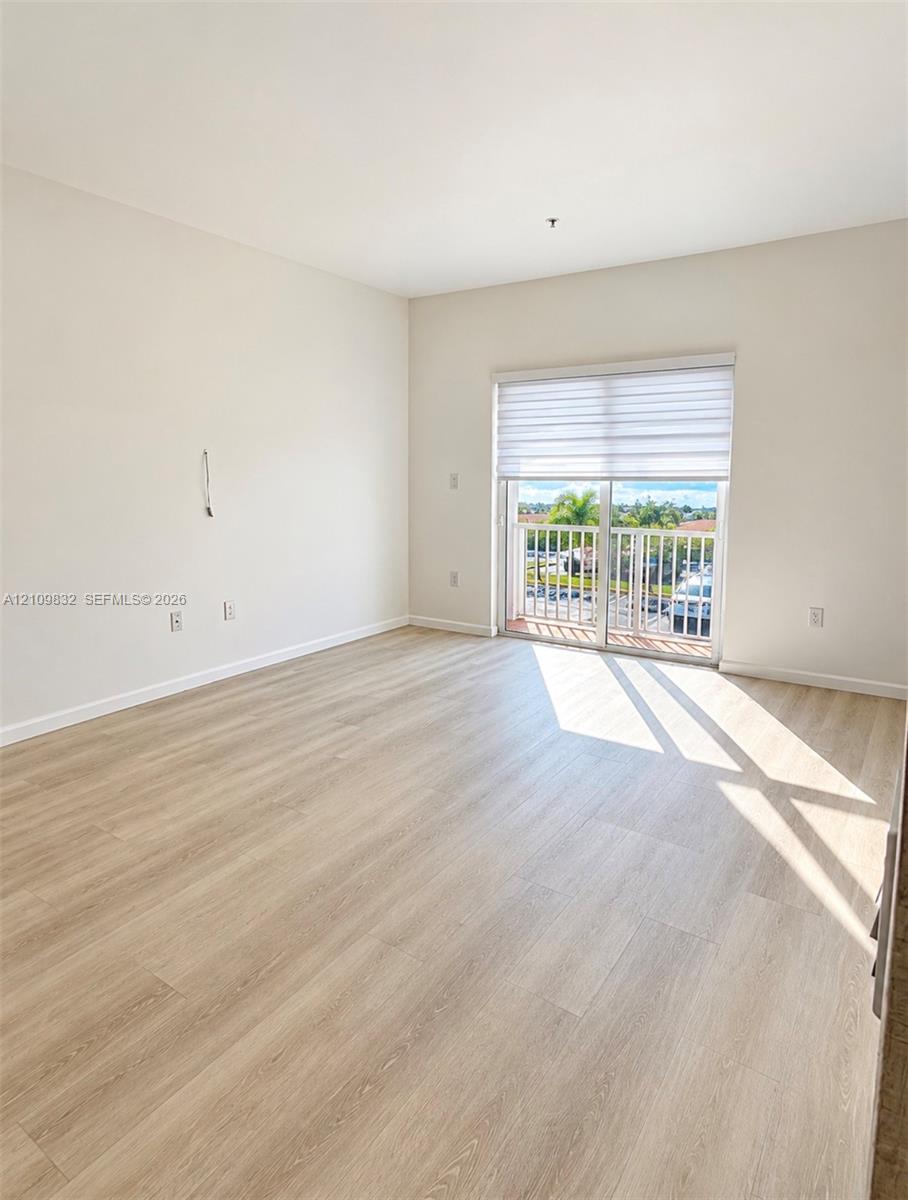 Light-filled room featuring wood-finish flooring, neutral wall paint, and sliding glass doors with an integrated shade opening to an exterior balcony