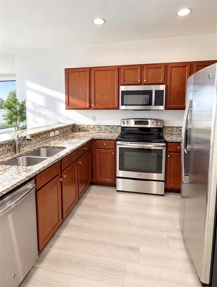 Kitchen featuring wood cabinetry, stone-finish countertops, stainless steel appliances, a double-basin undermount sink, and wood-finish flooring Kitchen featuring wood cabinetry, stone-finish countertops, stainless steel appliances, a double-basin undermount sink, and wood-finish flooring