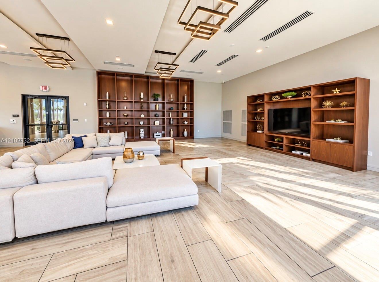 Large open-concept space featuring wood-finish flooring, floor-to-ceiling built-in wood shelving, and tiered geometric pendant lighting