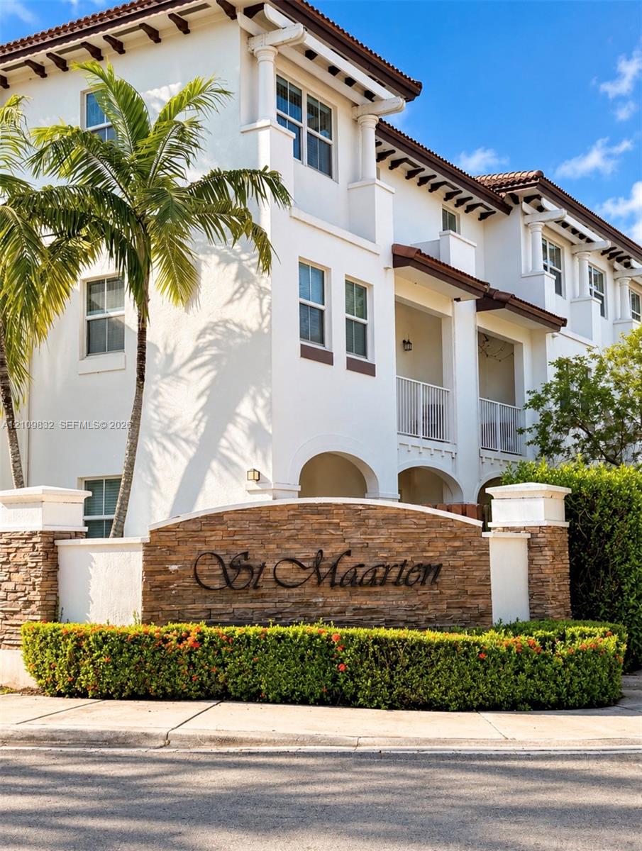 Stucco exterior featuring arched architectural detailing, private balconies with white railings, stone veneer signage, and mature palm landscaping