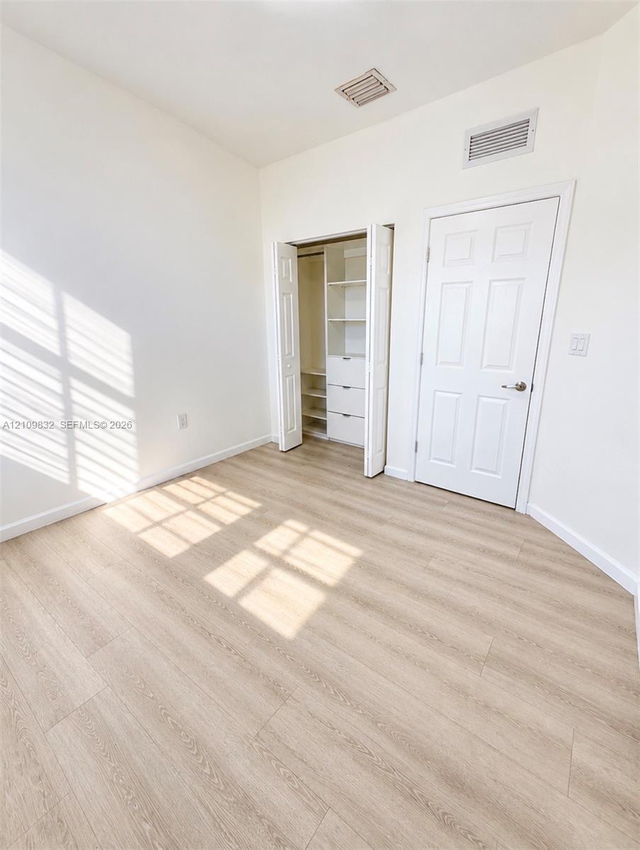 Room featuring wood-finish flooring, a six-panel interior door, and a built-in closet with integrated shelving and drawer storage