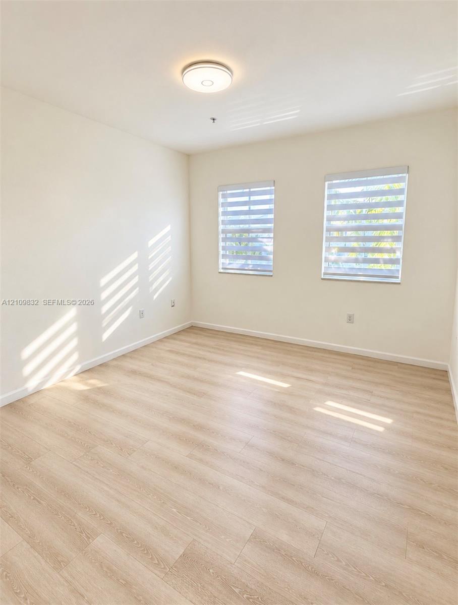 Neutral-toned interior space featuring wood-finish flooring, dual windows with installed roller shades, and a flush-mount ceiling light fixture