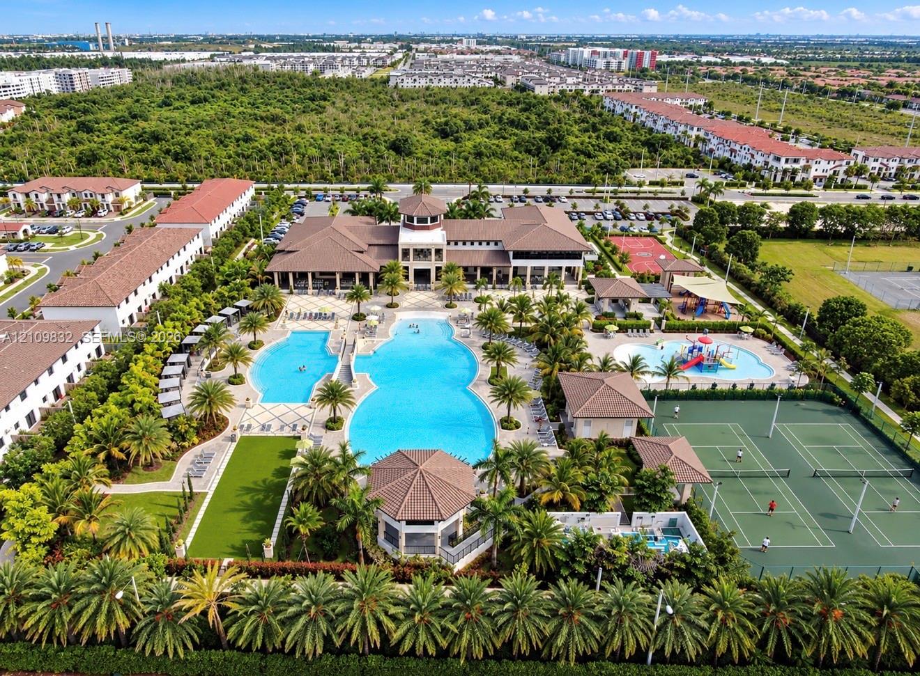 Community recreation complex featuring a large resort-style swimming pool, multiple tennis courts, a splash pad, and a clubhouse with a central tower