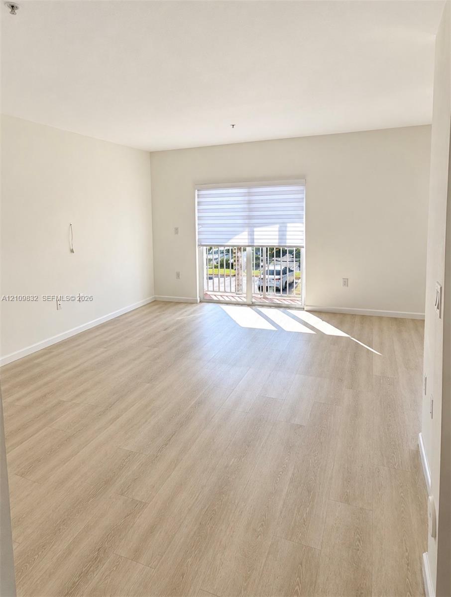 Open-concept living space featuring wood-finish flooring, neutral wall paint, and a sliding glass door providing access to a private balcony