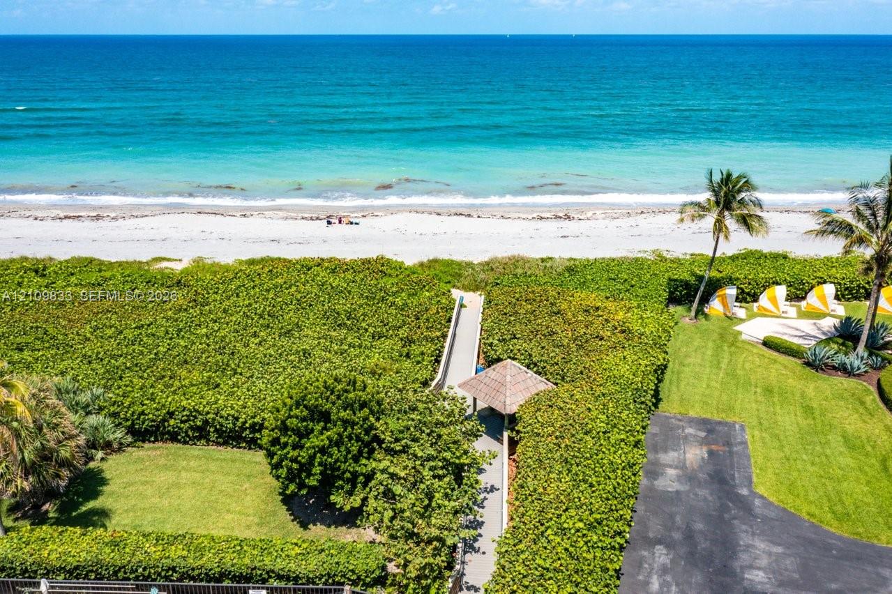 Oceanfront property featuring direct beach access via a private boardwalk, a covered gazebo, mature tropical landscaping, and a manicured lawn