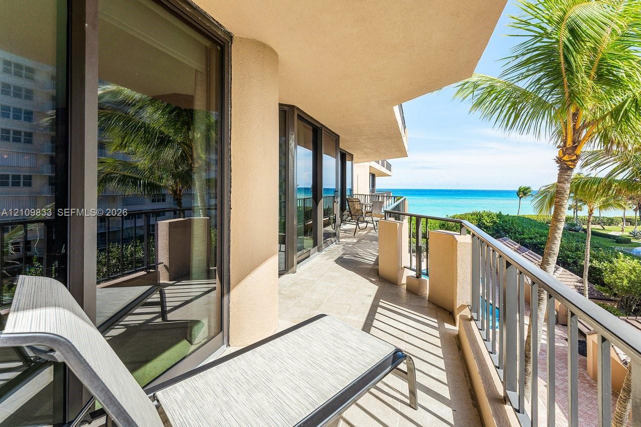 Covered balcony featuring tile flooring, full-height glass sliding doors, and metal railings, overlooking the ocean