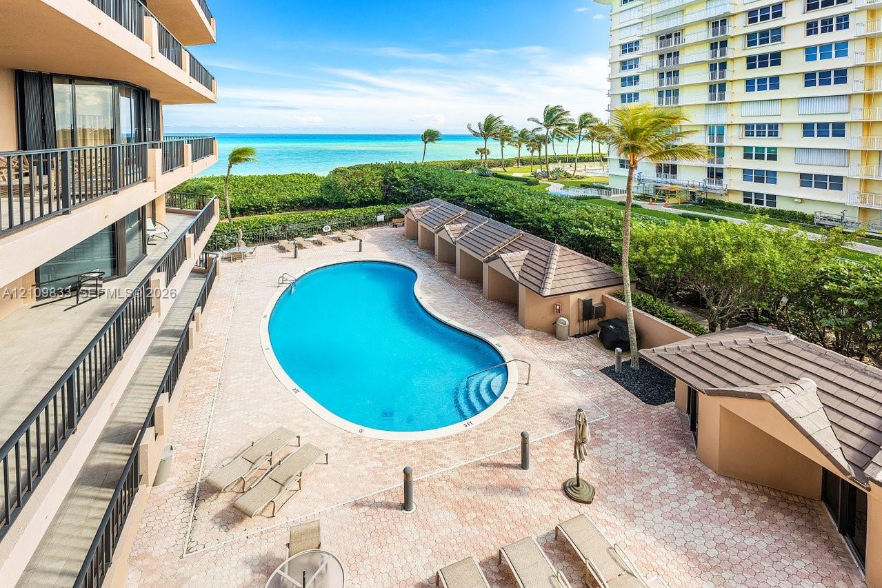 Community pool area featuring a kidney-shaped swimming pool, paver deck, covered cabanas with tiled roofs, and direct oceanfront presence