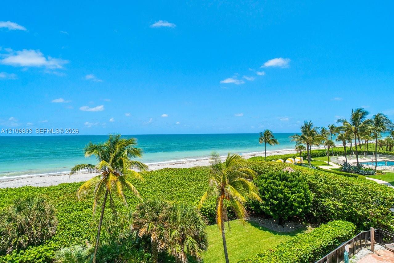 Coastal property featuring direct ocean frontage, manicured landscaping with mature palms, and an outdoor swimming pool
