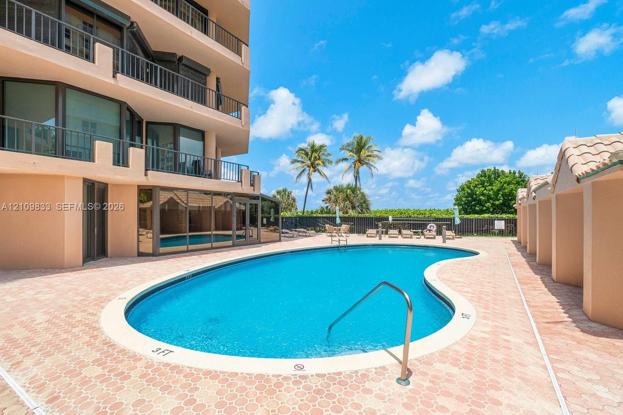 Swimming pool with a curved concrete deck, metal handrail, perimeter privacy fencing, and exterior balconies