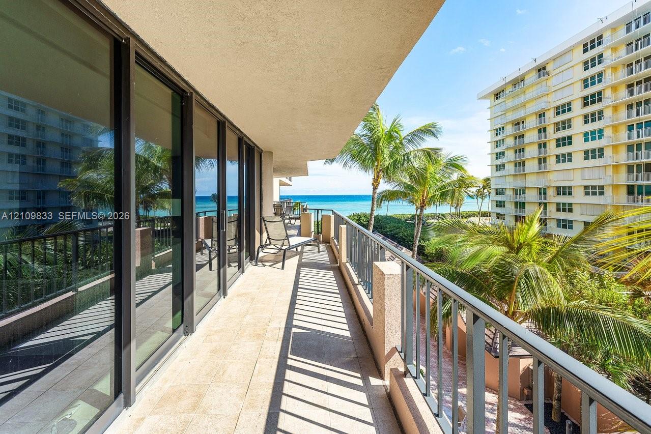 Covered balcony featuring tile flooring, full-height sliding glass doors, and metal railings with water and palm tree scenery