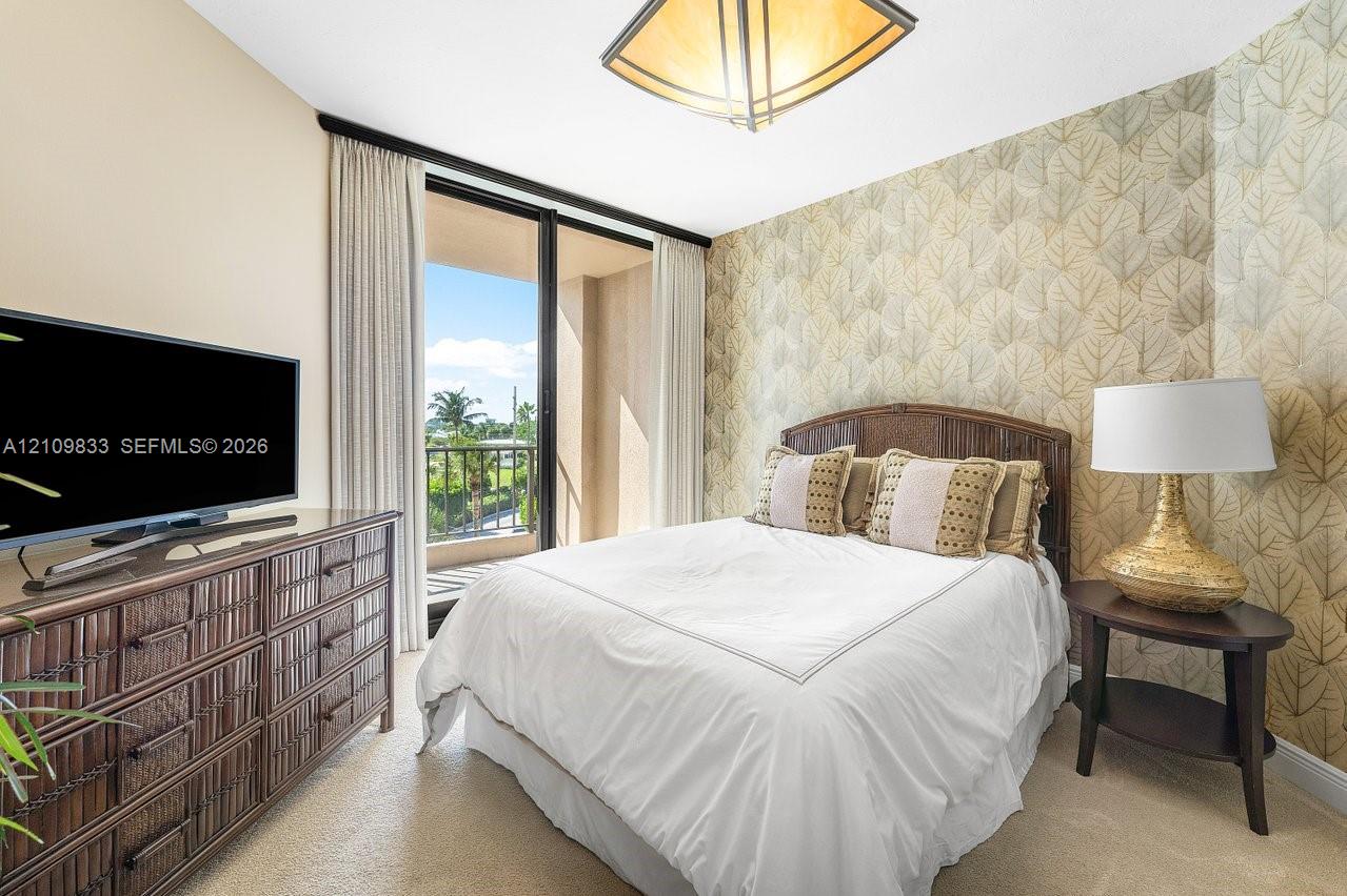 Floor-to-ceiling glass sliding doors opening to a private balcony, patterned wall covering, flush-mount geometric lighting fixture, and carpeted flooring