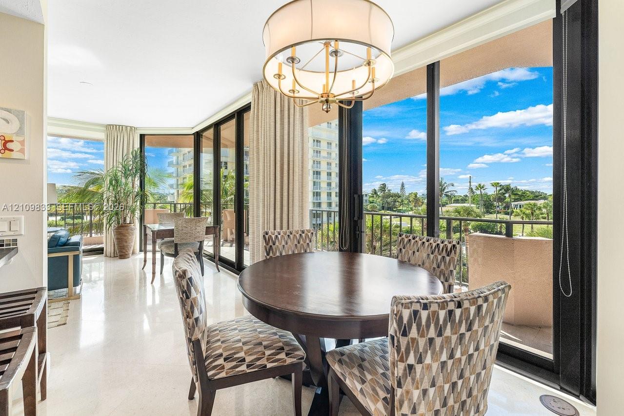 Floor-to-ceiling glass sliding doors, stone-finish flooring, metal-framed balcony railing, and a drum-style chandelier with brass-finish hardware