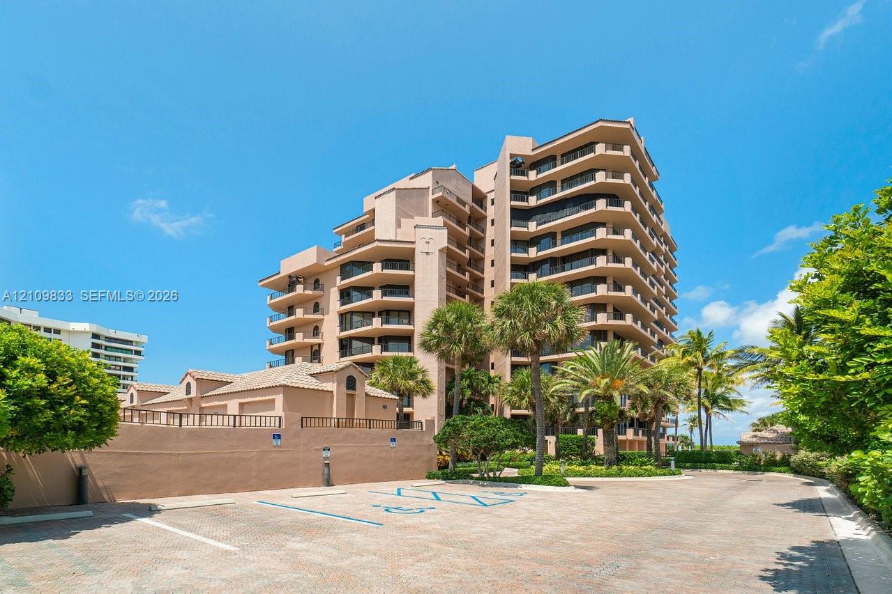 Multi-story high-rise building featuring private balconies, masonry exterior, paved parking area, and mature palm trees Multi-story high-rise building featuring private balconies, masonry exterior, paved parking area, and mature palm trees
