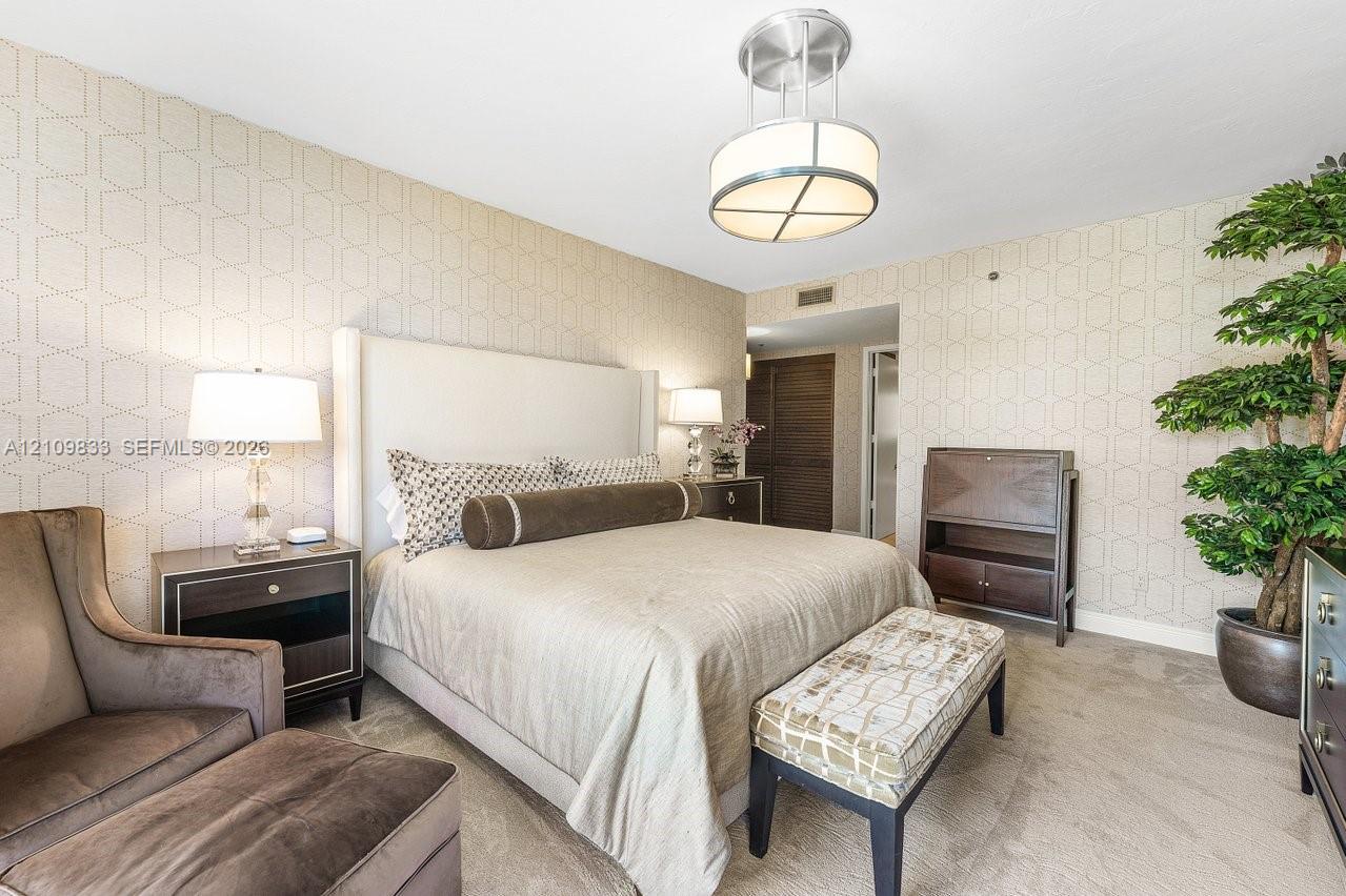 Geometric patterned wall covering, neutral-toned flooring, and a modern brushed-metal drum chandelier