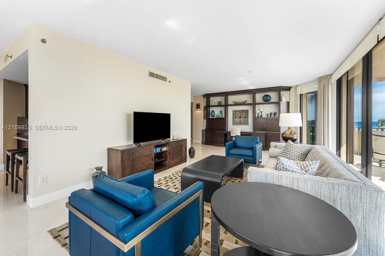 Open-concept interior featuring large-format stone flooring, floor-to-ceiling glass panel windows, and custom built-in dark wood shelving with integrated storage