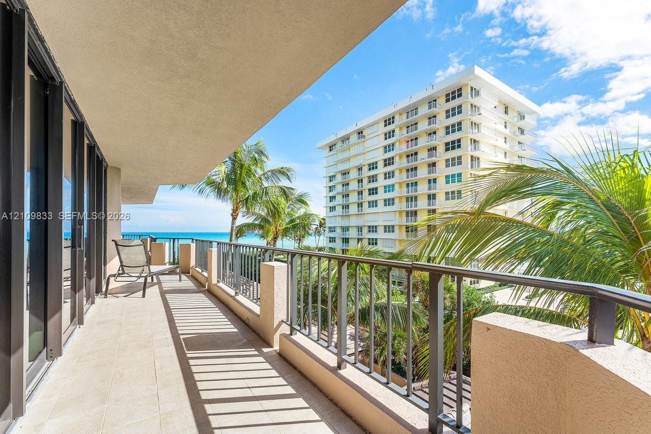 Covered balcony featuring tile flooring and metal railings, overlooking palm trees and the ocean