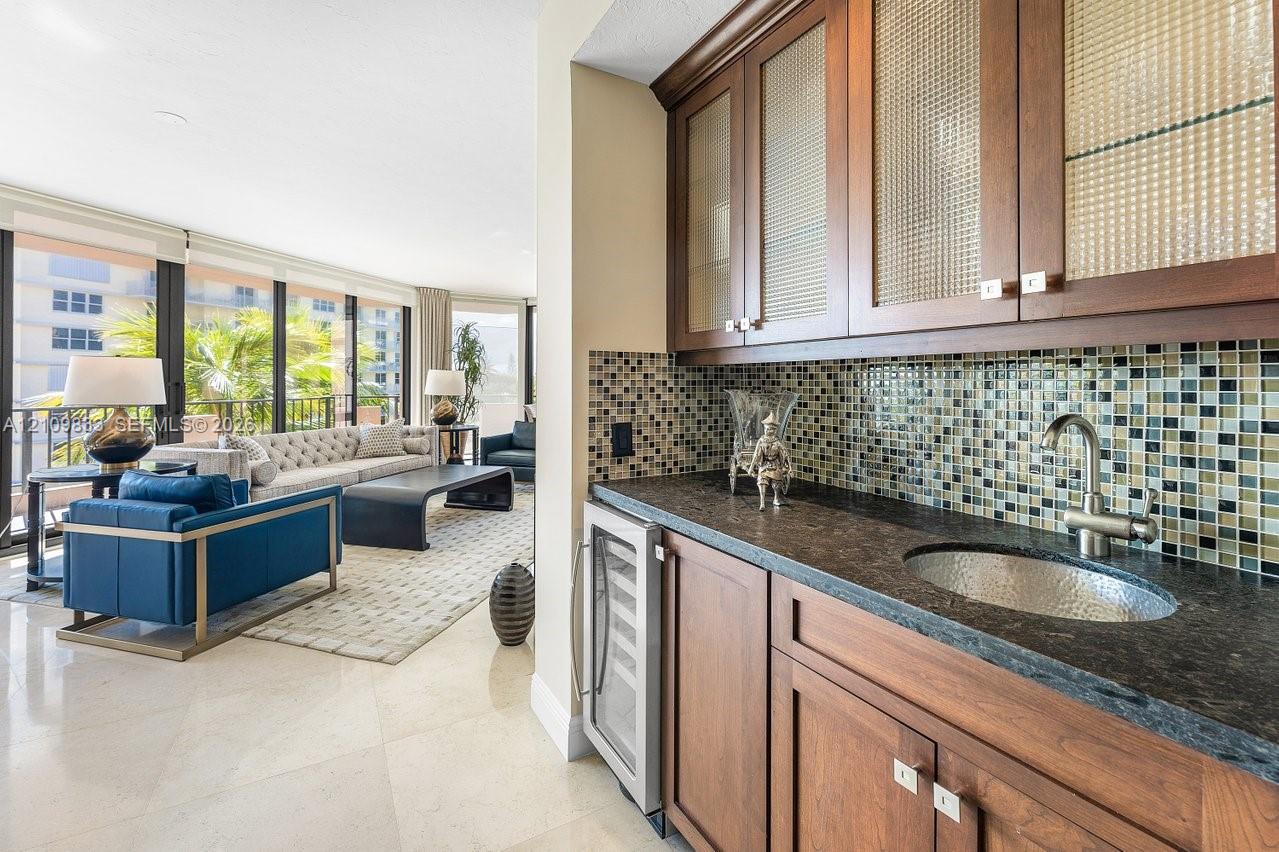 Wet bar featuring wood cabinetry, textured glass cabinet fronts, stone countertop, hammered metal sink, and mosaic tile backsplash Wet bar featuring wood cabinetry, textured glass cabinet fronts, stone countertop, hammered metal sink, and mosaic tile backsplash