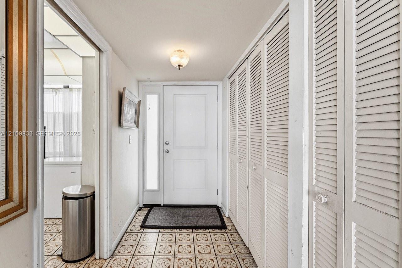Entryway featuring a white paneled door with a vertical glass sidelight, floor-to-ceiling white louvered-style closet doors, patterned tile flooring, and a globe-style flush mount ceiling light
