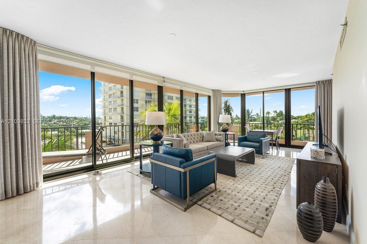 Floor-to-ceiling glass walls, polished stone flooring, and expansive wrap-around balcony with metal railing