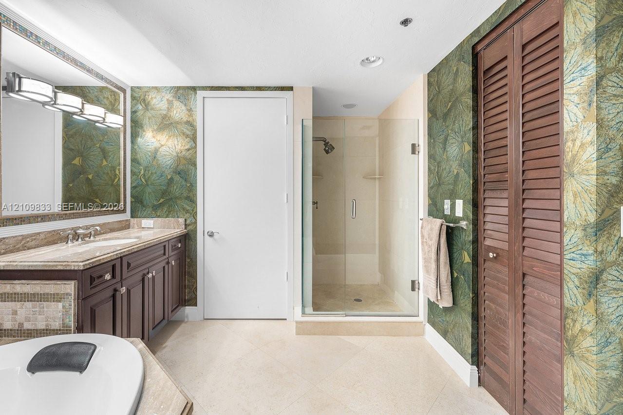 Bathroom featuring a dark wood-finish vanity with a stone countertop, an oversized wall mirror with decorative trim, a walk-in glass-enclosed shower, and floor-to-ceiling louvered-style wood closet doors
