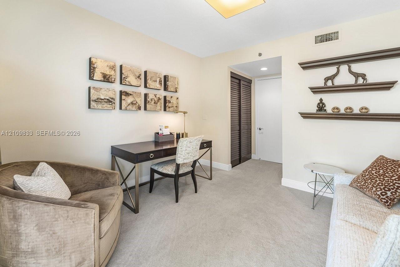 Room featuring neutral wall tones, wall-to-wall carpeting, recessed lighting, built-in wooden shelving, and a closet with louvered doors