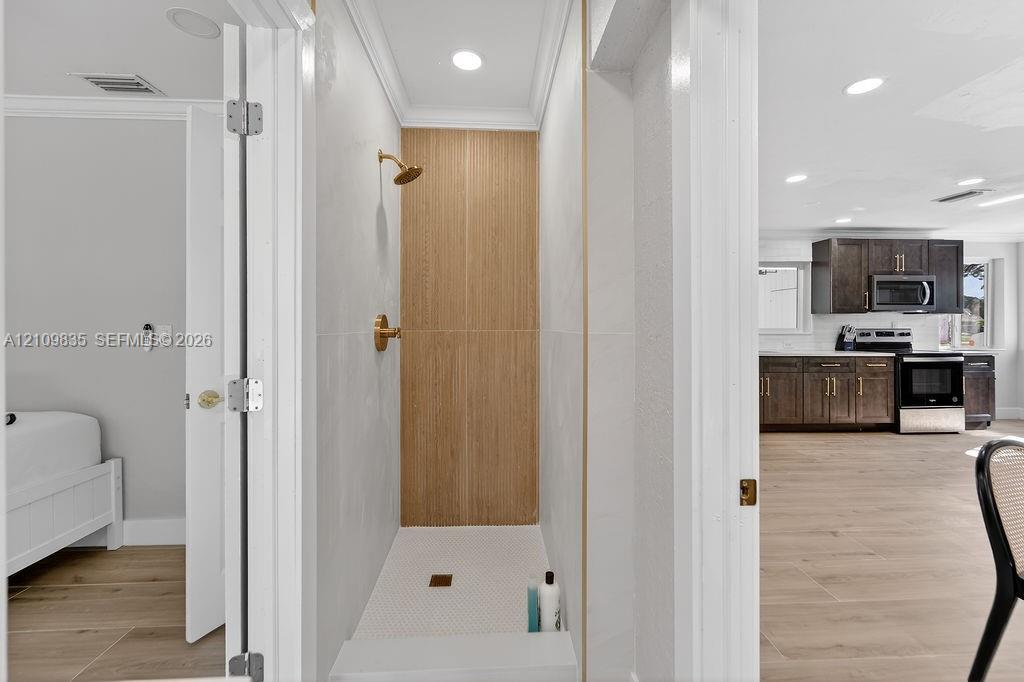 Walk-in shower featuring gold-toned fixtures, a wood-finish tile accent wall, white wall tiling, and recessed lighting