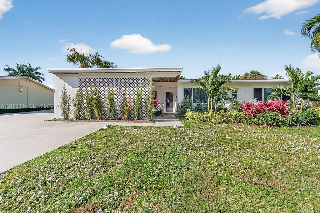 Single-story exterior featuring a flat roofline, decorative lattice screen, concrete driveway, and established tropical landscaping
