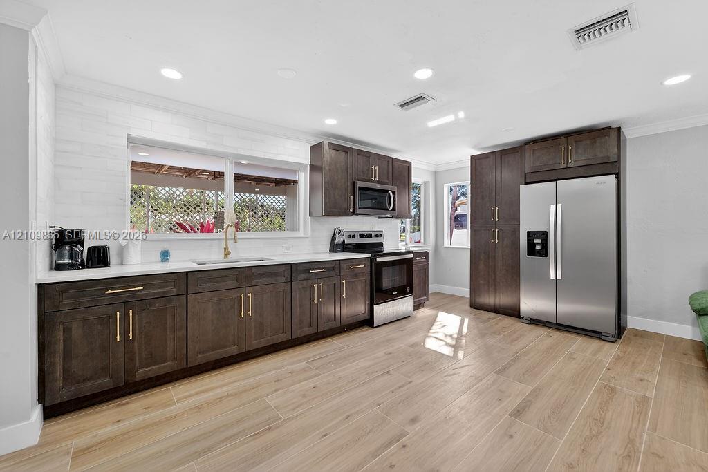 Kitchen featuring dark wood-finish cabinetry, white solid-surface countertops, wood-finish flooring, stainless steel appliances, and a white tile backsplash