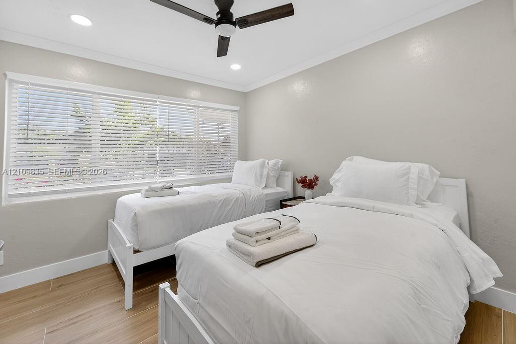 Room featuring wood-finish flooring, recessed lighting, crown molding, a multi-blade ceiling fan, and a large window with horizontal blinds