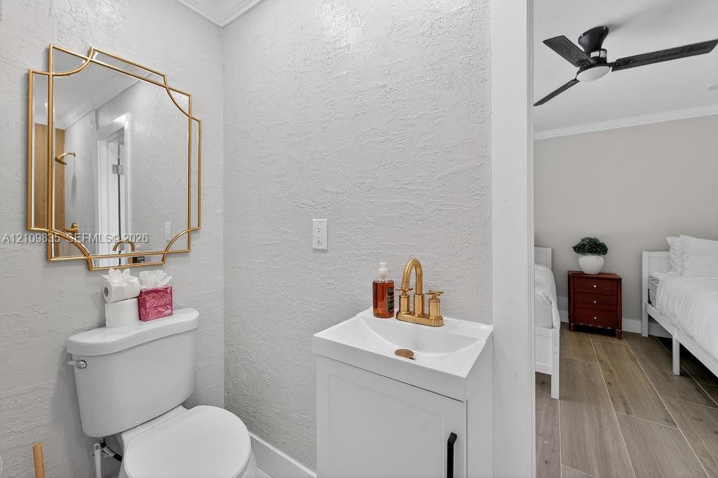 Bathroom featuring a geometric gold-framed mirror, white pedestal vanity with metallic gold hardware, bridge-style faucet, and wood-finish flooring